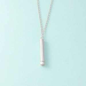 Vertical view of a silver cylindrical pendant on a delicate chain over blue background