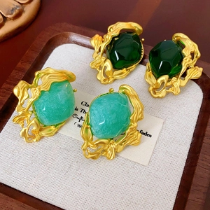 Detail of vintage gold earrings with emerald green and seafoam gemstones in a wooden tray
