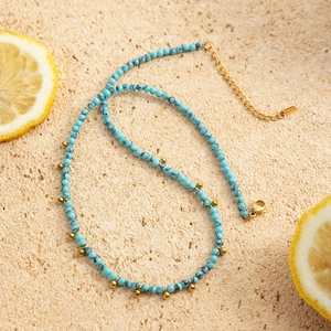 Blue turquoise bead necklace with gold accents on stone background with lemon slices
