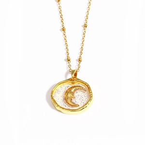 Close-up of golden beaded chain necklace with crescent moon embossed on resin pendant