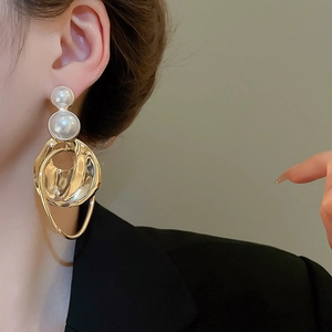 Detail view of irregular gold metal earrings with stacked white pearls worn by a model