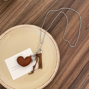 Close-up of vintage necklace featuring brown leather heart, wooden beads and silver bird charm
