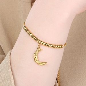 Adjustable gold beaded bracelet with a textured moon pendant worn on a model's wrist