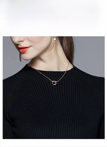 Gros plan d'un collier en or rose à cercles entrelacés sur un pull noir élégant