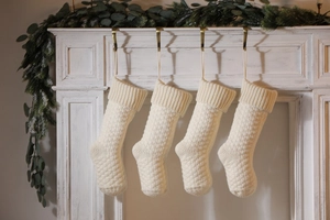 Close-up of four cream knitted Christmas stockings hanging on a fireplace mantel decoration