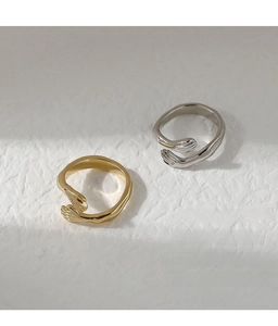 Detailed view of creative hand hug open rings in gold and silver on a textured surface