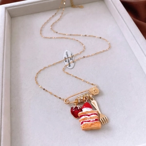 Macro shot of gold safety pin necklace with strawberry cake and fork charms