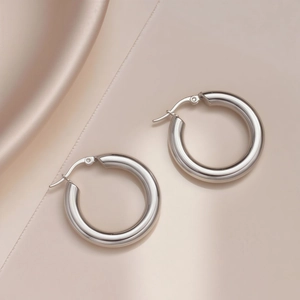 Detailed macro view of polished silver titanium steel hoop earrings on satin fabric