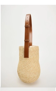 Detailed view of handmade woven straw bucket bag with adjustable brown leather shoulder strap