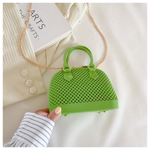 Detail of green PVC shell bag with textured surface and gold chain strap held by hand