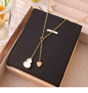 Detail of 18k gold plated necklace with gourd and heart pendants on a black jewelry stand