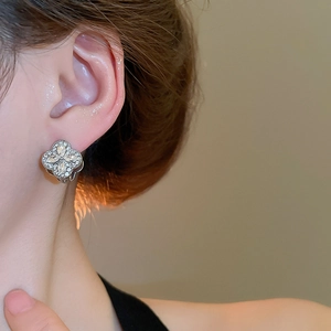 Close-up of sparkling silver clover earrings with inlaid diamonds worn on ear