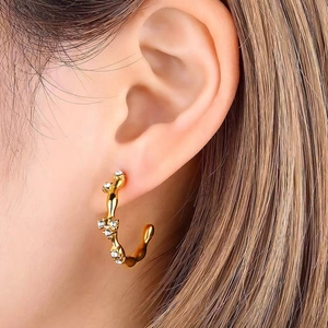Close-up of gold geometric C-shaped hoop earrings with white zircons on a model's ear