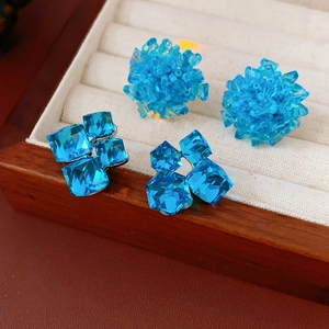 Macro detail of teal crystal flower cluster and geometric square cut stud earrings