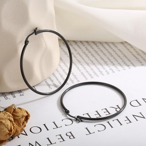 Detail of large black stainless steel hoop earrings displayed on a white ceramic vase