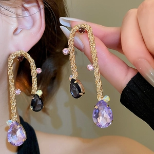 Dettaglio orecchini vintage dorati intrecciati con gemme a goccia viola e nere su modella