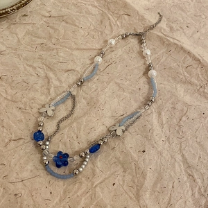 Detail of beaded necklace with blue flowers, silver butterfly charms and seed beads