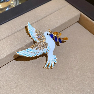 Detailed macro shot of white enamel peace dove brooch with blue crystals and olive branch