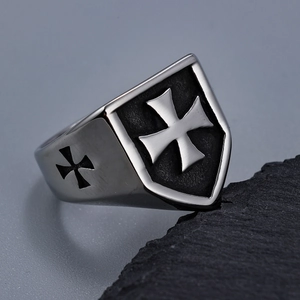 Detailed close-up of a vintage steel shield ring with a cross on a dark rock