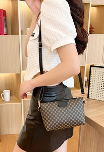Detail of a brown monogram shoulder bag with gold hardware worn by a model in a cozy setting