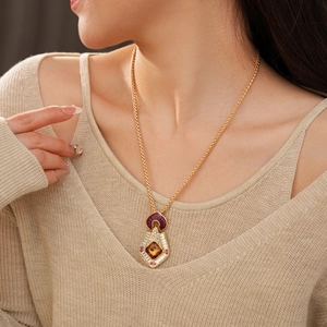 Close-up of vintage gold necklace with red and amber stones on a beige sweater