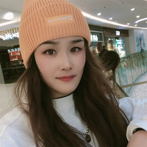 Close-up of bright orange knitted beanie featuring embroidered letter patch and folded cuff