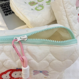 Detail of cream quilted makeup bag featuring heart patterns and colorful embroidery