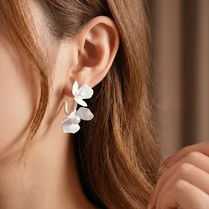 Elegant C-shaped pearl flower earrings with white matte petals on a female model