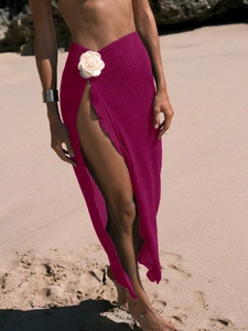 Detail of pink crochet beach skirt featuring a white floral ornament and high slit