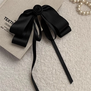 Elegant black satin ribbon hair clip with rose decoration on a linen book background