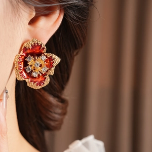 Close-up of vintage enamel flower earring with red petals and crystal center on model