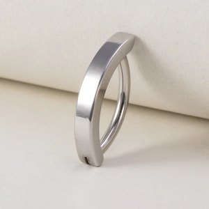 Close-up of a curved silver stainless steel navel ring on a soft textured background
