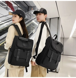 Modern black nylon backpack with flap design and decorative leather straps worn by couple
