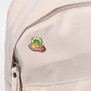 Cartoon frog in a UFO metal enamel pin attached to a beige canvas backpack strap
