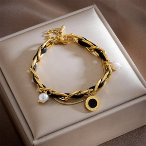 Detail of gold metal and black leather woven bracelet with pearl and roman disc charms