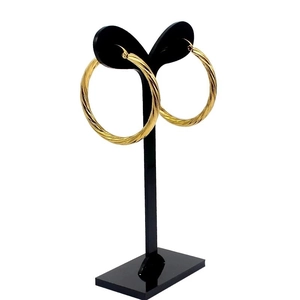 Golden stainless steel round hoop earrings with twisted thread design on a black stand