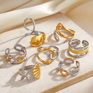 Two-tone stainless steel rings with starfish and chain designs on a stone surface