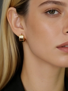 Close-up of elegant wide golden C-shaped hoop earrings worn by a model