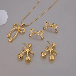 Elegant gold bow and cherry jewelry set including necklace and earrings on grey surface