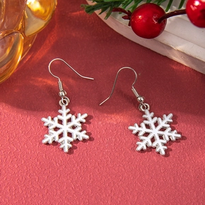 Macro shot of white enamel snowflake drop earrings on a festive red background