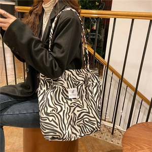 Detail of a large corduroy zebra pattern tote bag with slogan patch worn on the shoulder