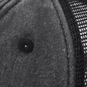 Macro detail of breathable black mesh and dark grey fabric stitching on a trucker hat