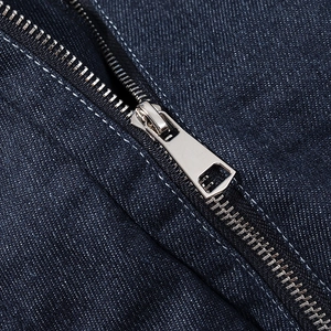 Macro shot of silver metal zipper and white stitching on dark blue denim jacket fabric
