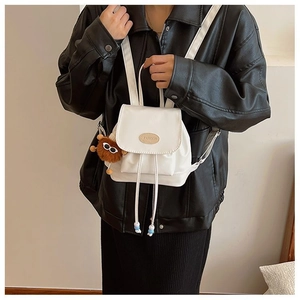 Close-up of a white mini PU backpack with a brown plush charm on a model in a black jacket