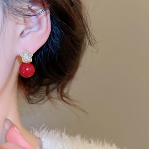 Close-up of gold star earrings with sparkling zircon and a glossy red pearl drop