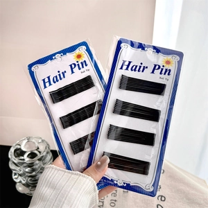 Black metal bobby pins with ball tips on card packaging held by a hand