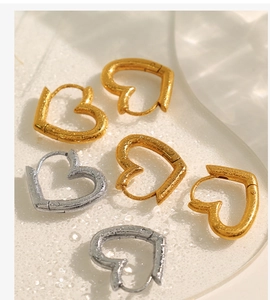 Detail shot of heart-shaped gold and silver earrings on a textured water-drop surface