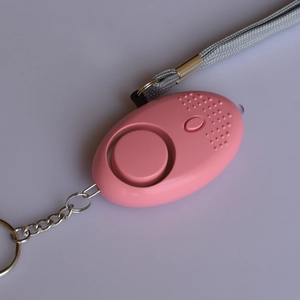 Pink personal alarm with metal keychain and grey wrist strap on a flat surface