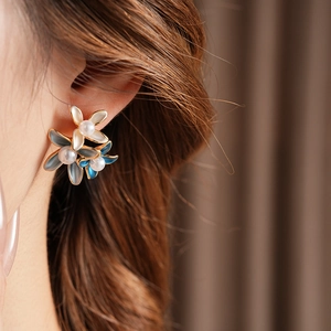 Detail of flower earrings with gold plating, pearl centers, and white petals on model