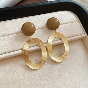Detail view of brushed gold oval earrings with brown resin beads on beige velvet pad